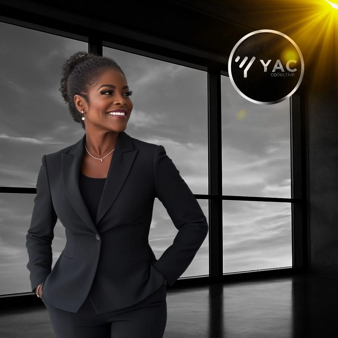 A Black woman stands in front of an office window, gazing thoughtfully at the glowing YAC Collective logo illuminated behind the glass.